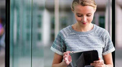 Young woman standing outside checking her tablet. Our products are essential in the production of semiconductors and are used in applications like solar cells, LEDs, smartphones and tablets. 